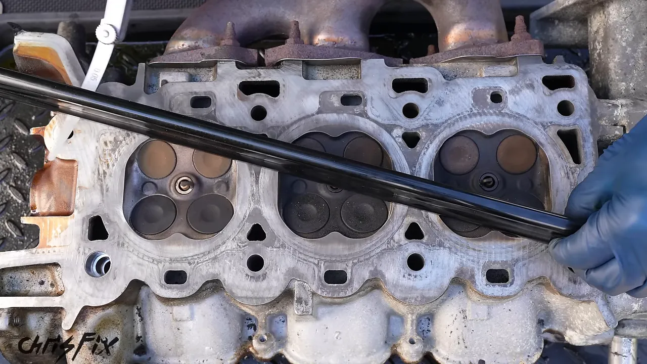 A feeler gauge being inserted beneath a straightedge laid diagonally across a cylinder head