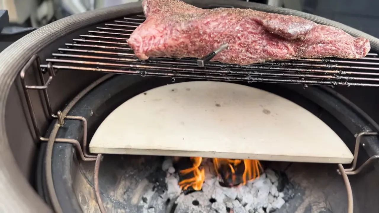 Meat on a raised half grate above a ceramic half-moon deflector with the fire visible below