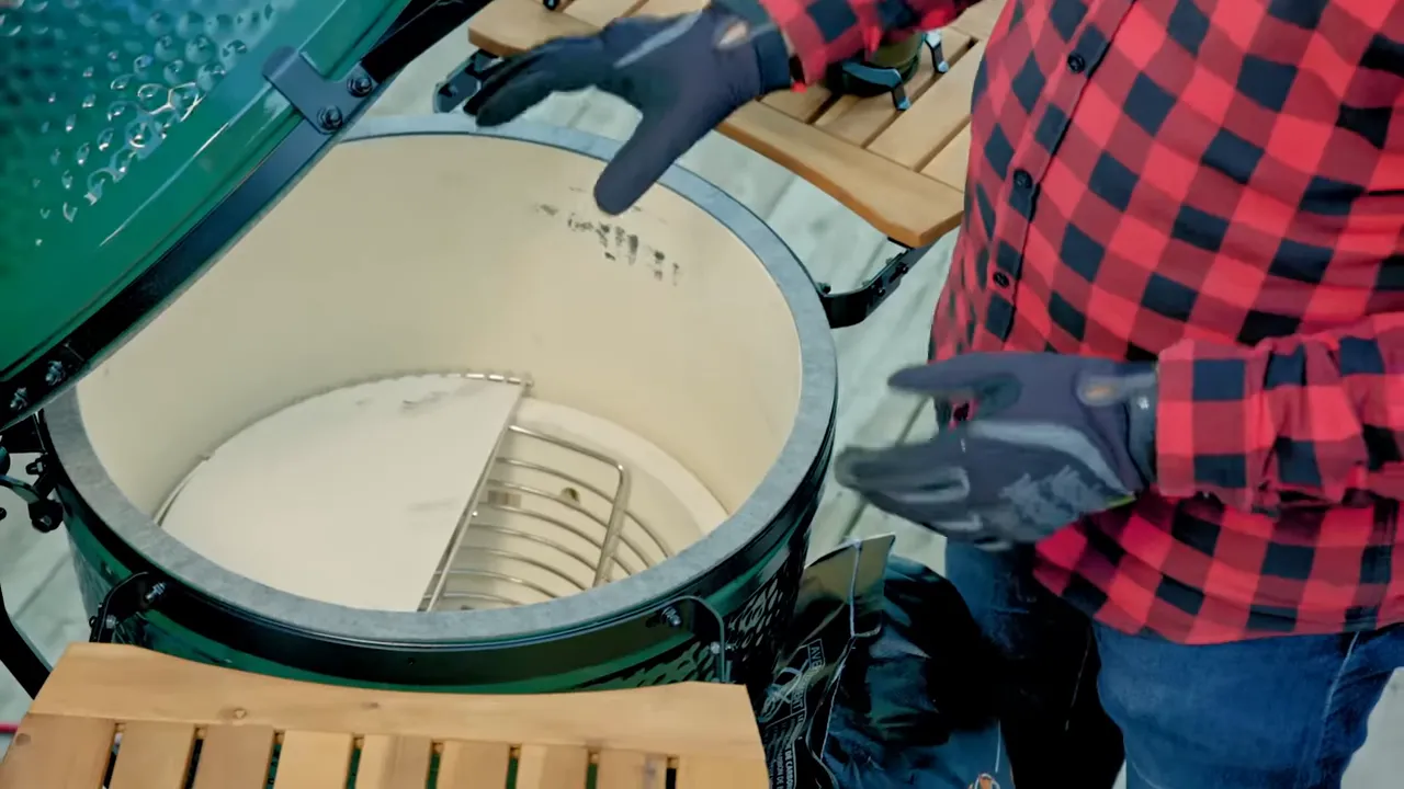 Open Big Green Egg showing a half-moon ceramic deflector beside an exposed section of charcoal basket