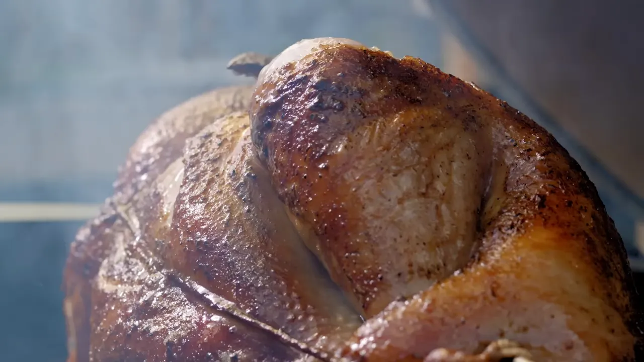 Golden-brown turkey rotating on a spit inside an open grill with smoke around it