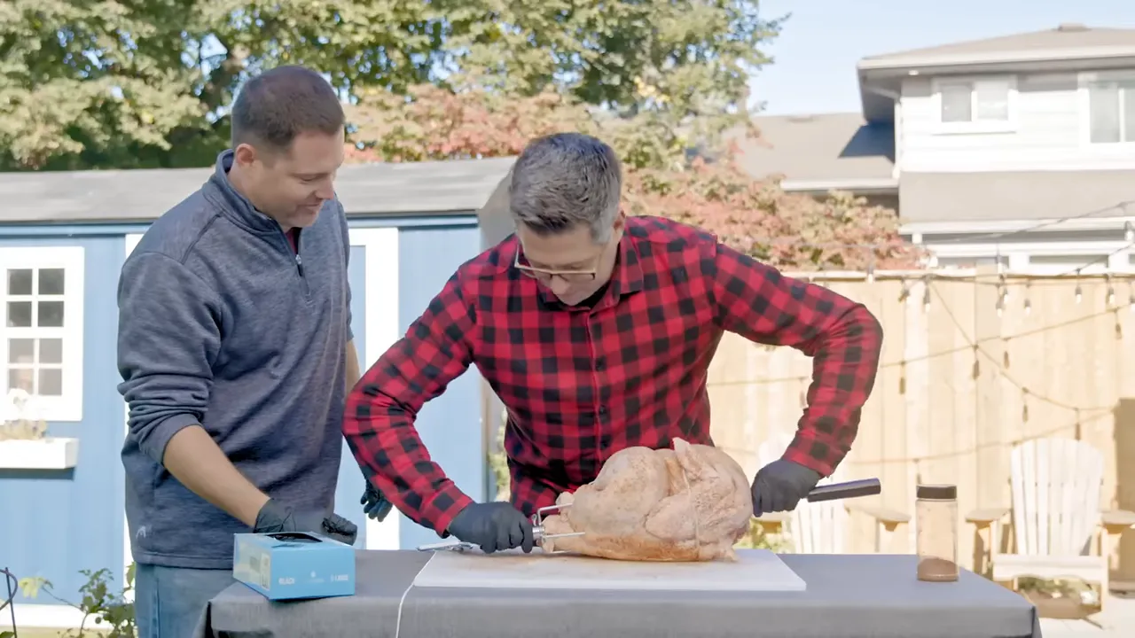 A seasoned turkey on a rotisserie spit with twine being tied around the bird and fork assembly