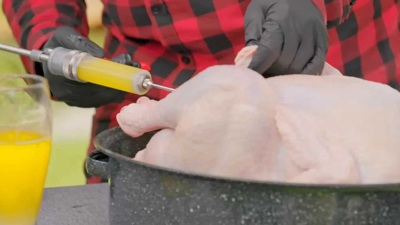 Gloved hands injecting yellow butter into a turkey breast in a roasting pan