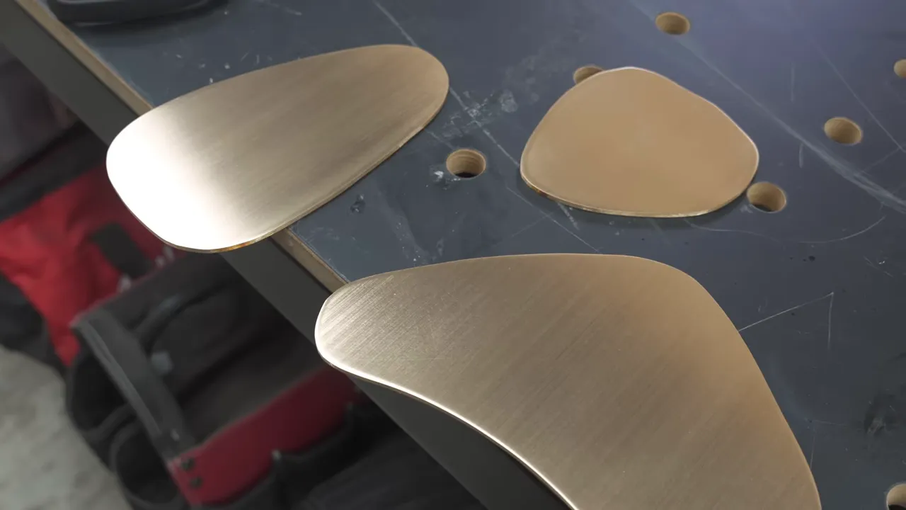 Several fitted bronze shapes with directional sanding lines on a dark work surface