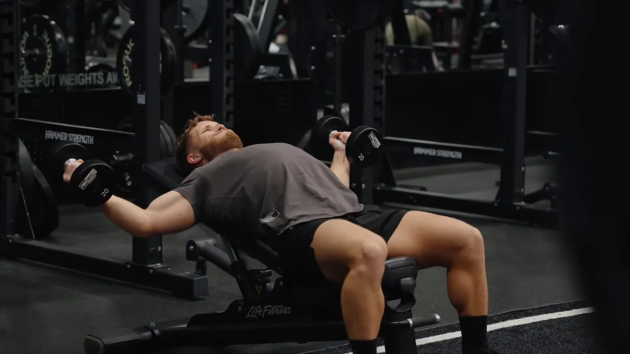 Incline dumbbell fly demonstration with arms spread and dumbbells lowered beside the bench