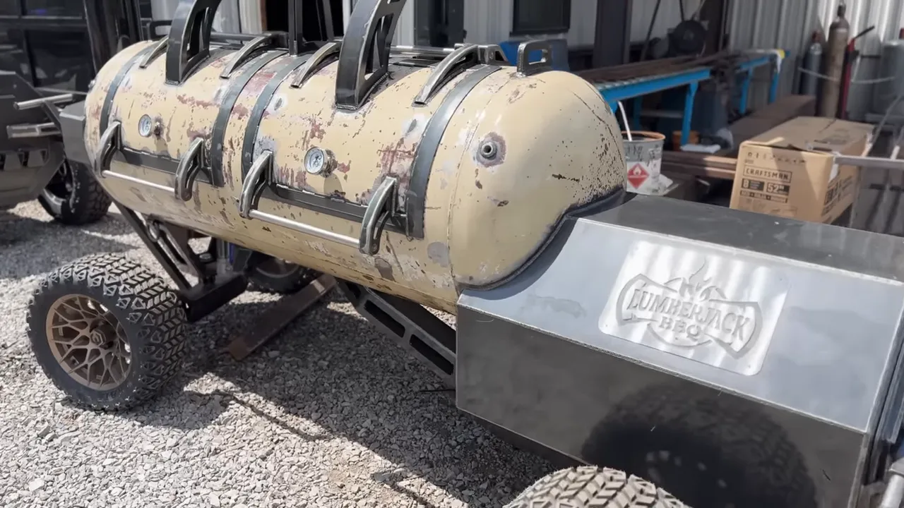Cream patina tank smoker with sculpted metal hinges, an angular firebox, and large treaded tires