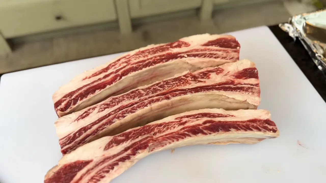 Three individual raw beef ribs arranged on a white cutting board