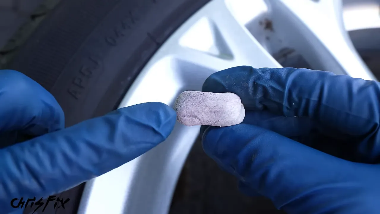 Blue-gloved hands holding a small piece of clay with dark contamination marks