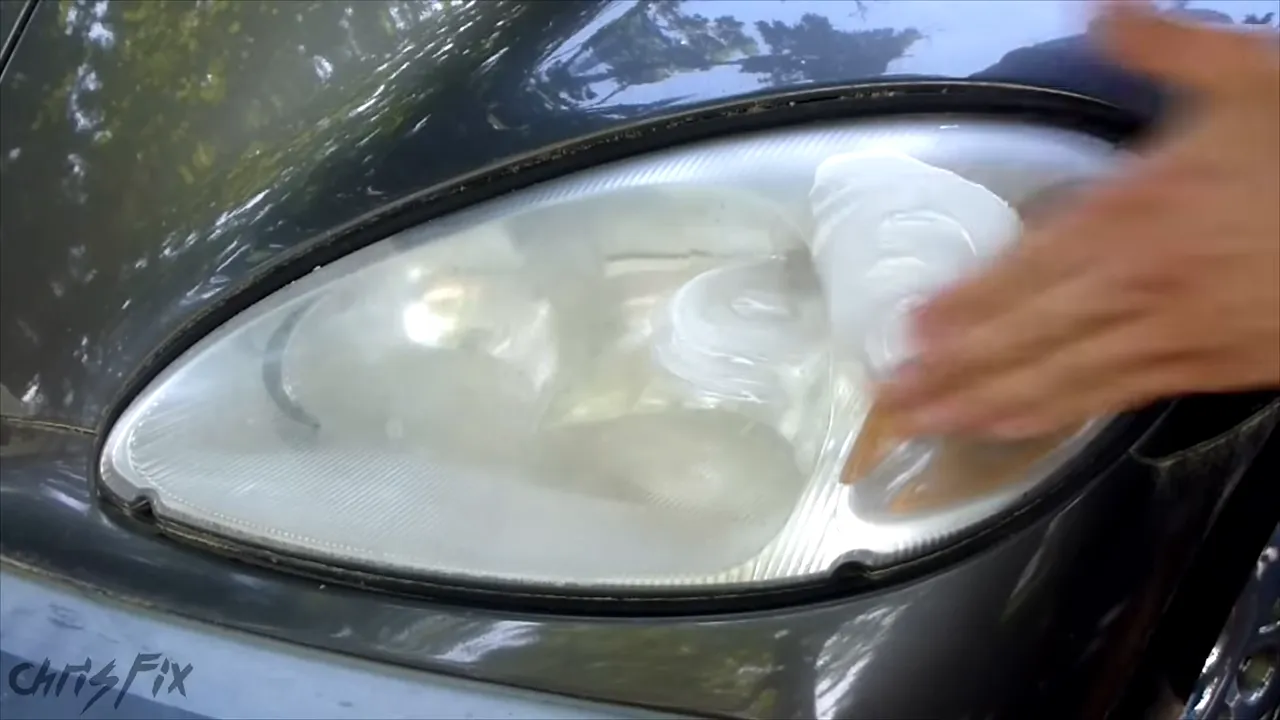 Hand spreading white toothpaste over the headlight lens