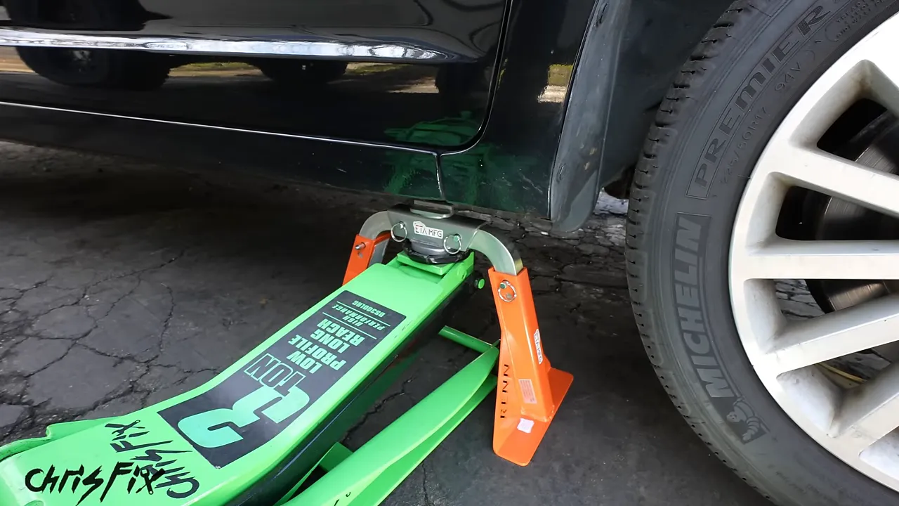 Green floor jack beneath a car with orange jack stand legs positioned on either side