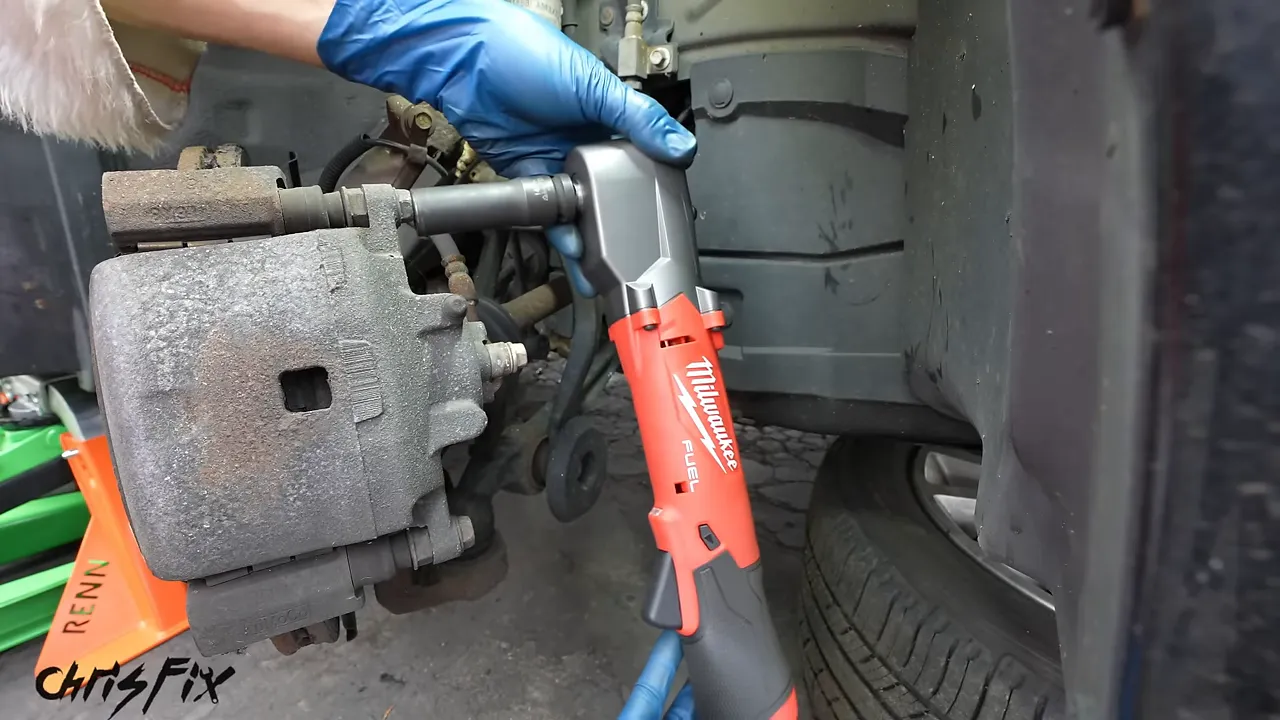 Blue-gloved hands positioning a slim red right-angle impact tool beside a brake assembly