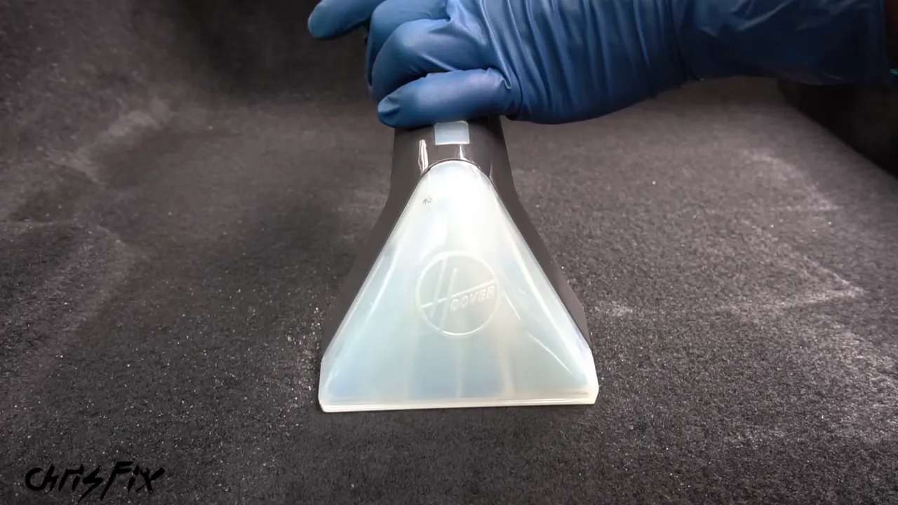 Clear extractor nozzle pulling liquid from dark automotive carpet