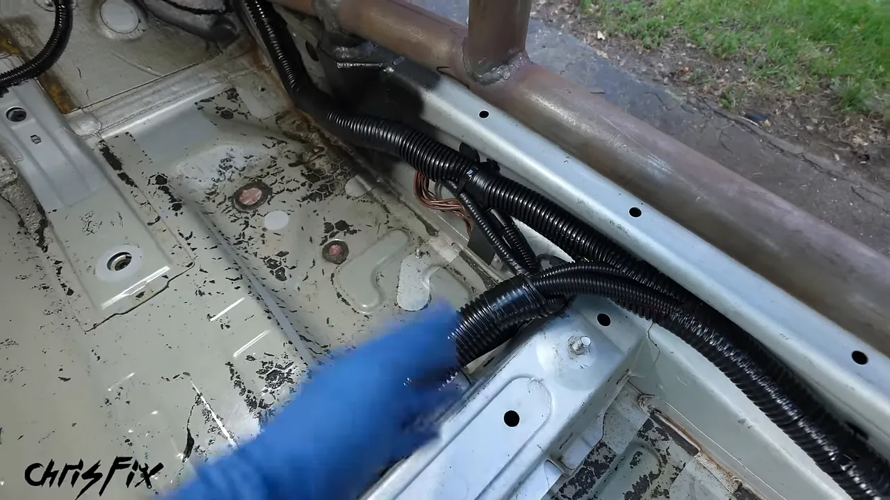 Protected black cable looms secured along the bare passenger-side floor and seat crossmember