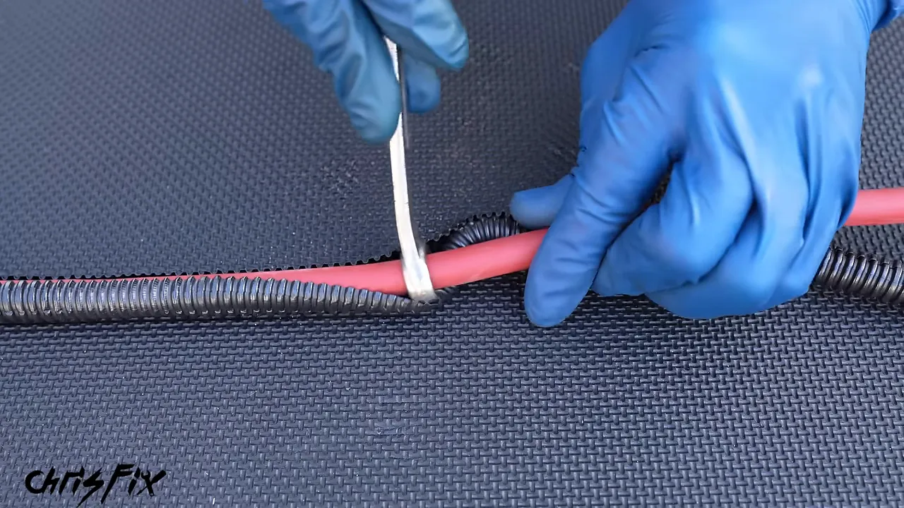 Box-end wrench guiding red battery cable into black split wire loom