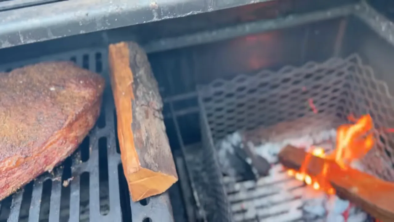 Brisket on the left cooking grate beside a wood split burning in the right-side mesh basket