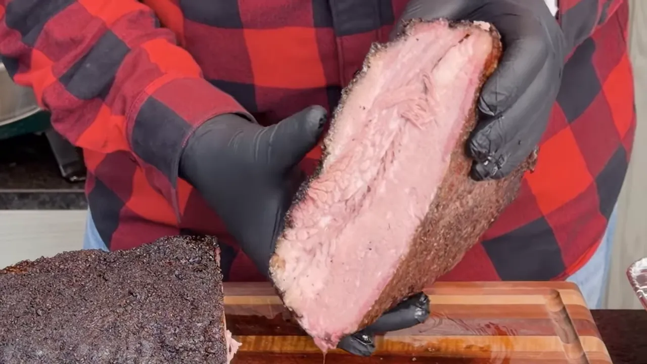 Gloved hands holding a cut brisket section with its interior and dark bark visible