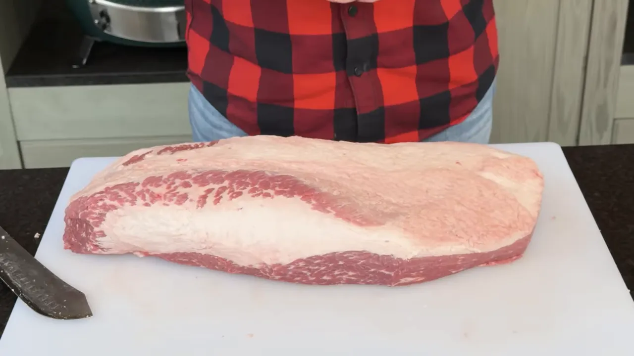 Trimmed raw brisket with a smooth fat cap on a white cutting board