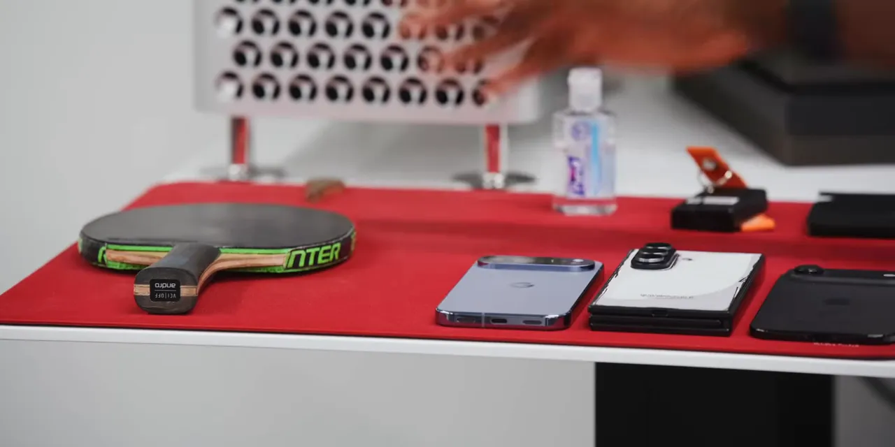 Red desk mat holding three phones, a table tennis paddle, keys, a wallet, and hand sanitizer