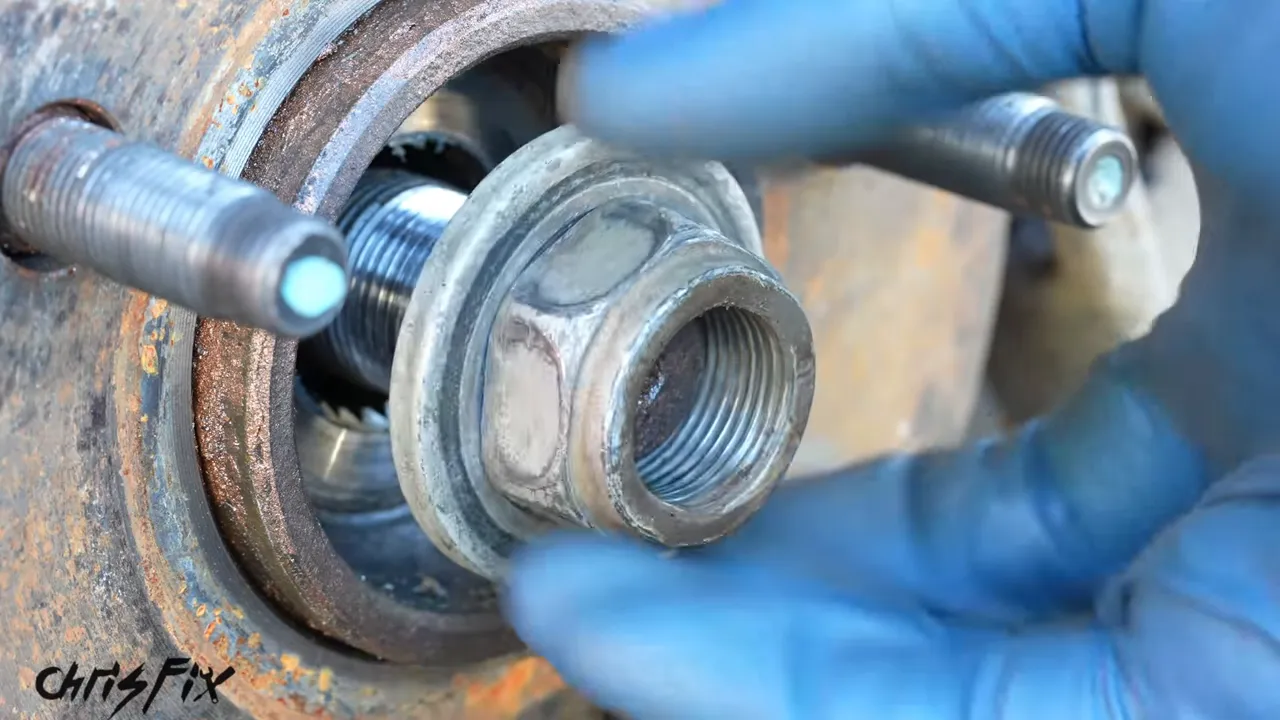 Gloved hands removing the axle nut and washer from the threaded axle end