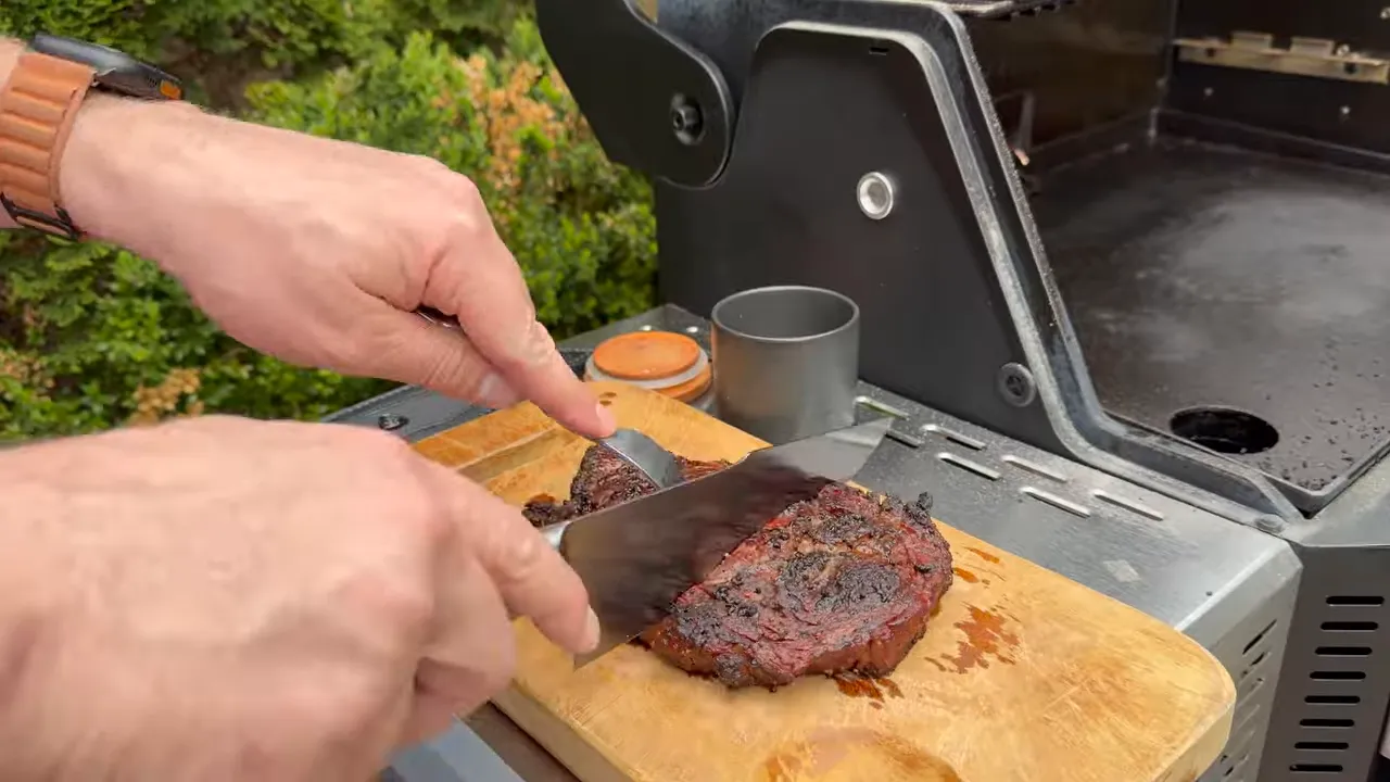 Steak being sliced on a cutting board beside an open Masterbuilt griddle
