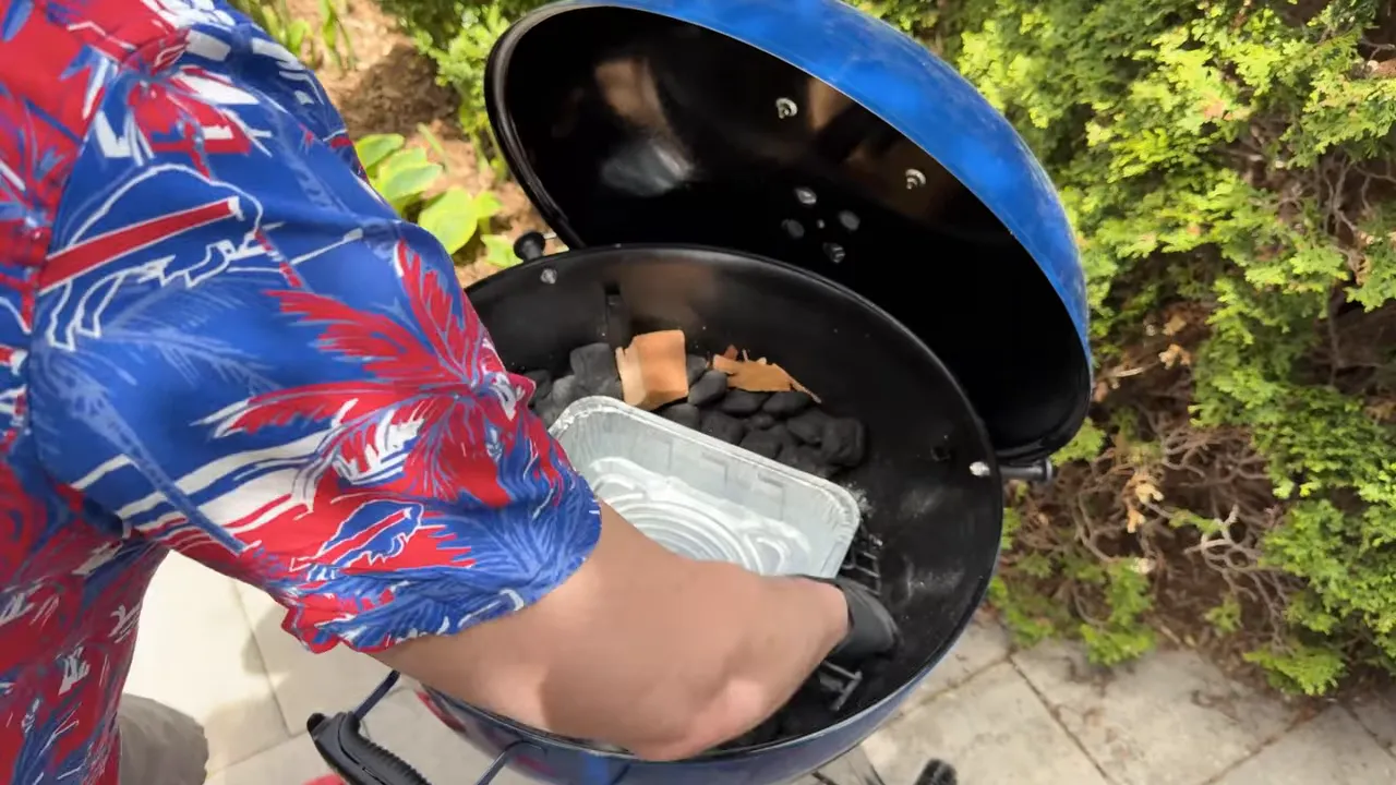 Briquettes and wood chunks arranged around a foil pan inside an open Weber Kettle