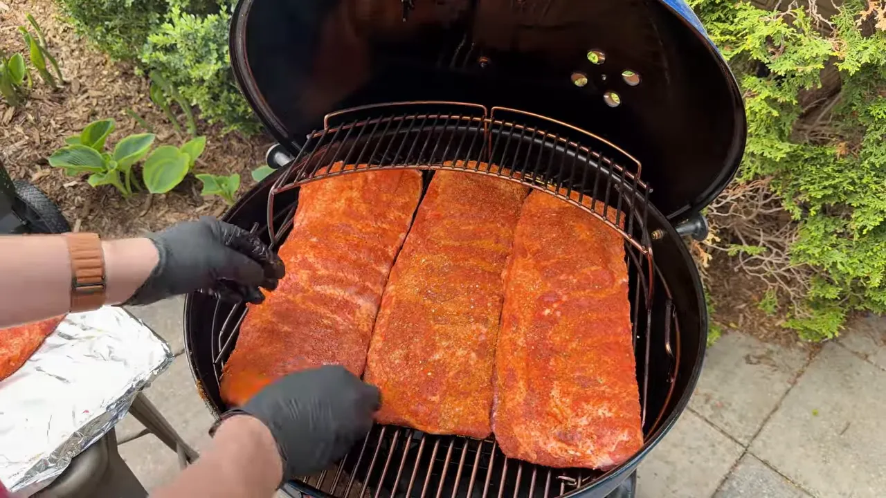 Three seasoned racks of ribs laid side by side on a Weber Kettle cooking grate
