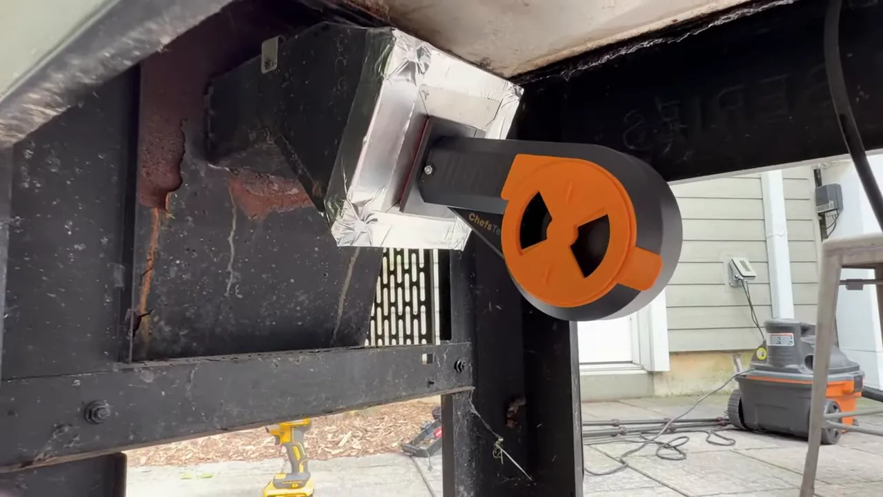 Black and orange Breezo fan mounted in a foil-taped metal adapter under the grill