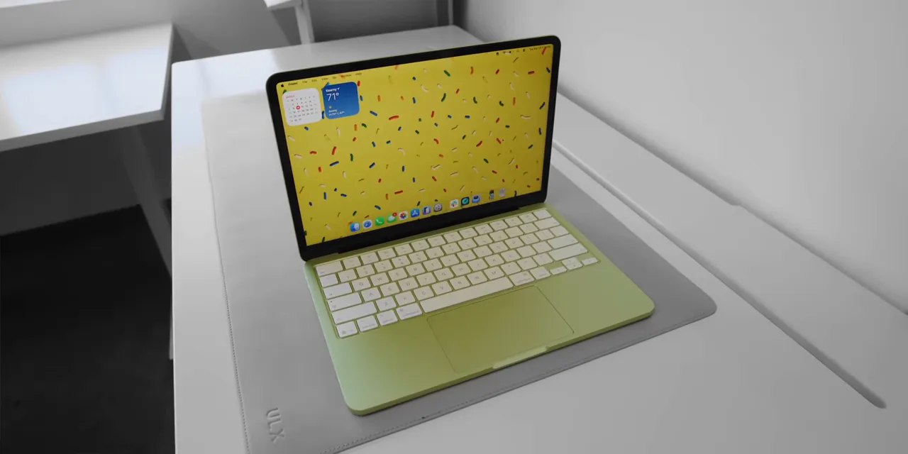 Yellow-green MacBook Neo open on a white surface with its keyboard and desktop visible