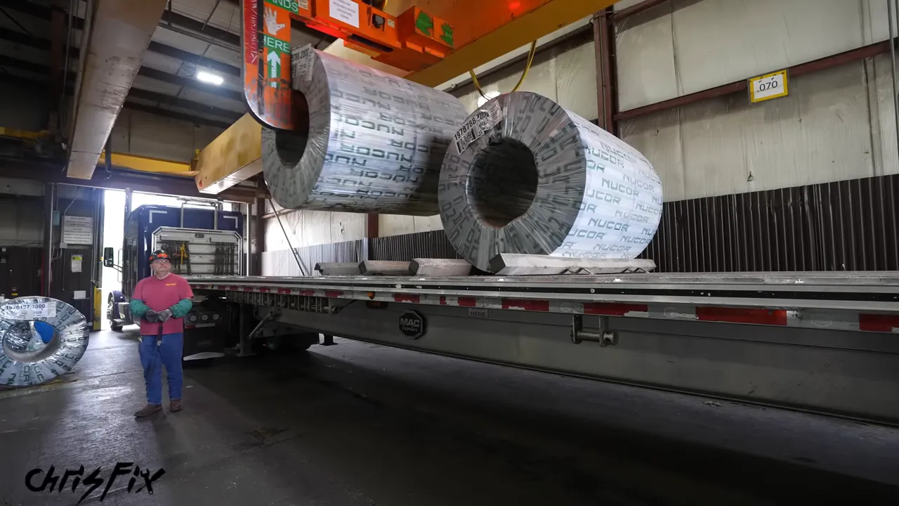 Overhead crane lifting a wrapped steel coil from a flatbed trailer