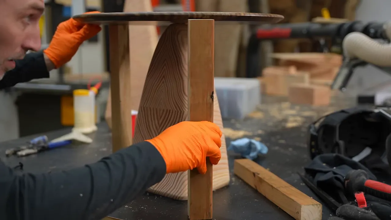 A round tabletop supported above a tapered fir base by wooden spacer sticks