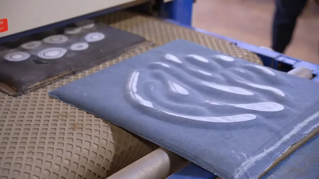 A surfaced denim panel with pale curved patterns on the conveyor of a wide belt sanding machine