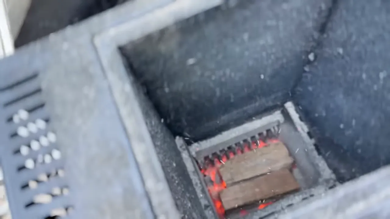 Small wood split resting over glowing coals at the bottom of the Gravity XT hopper
