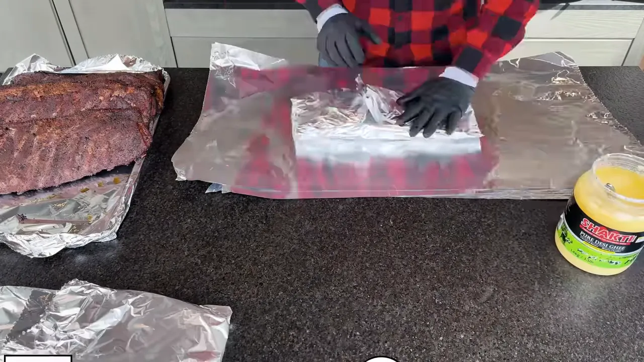 Gloved hands placing a rib rack meat-side down over yellow ghee on foil