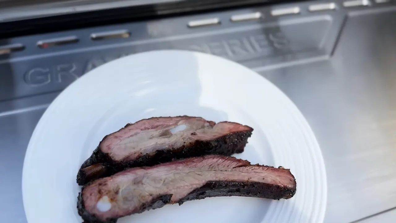 Two sliced ribs on a white plate showing the meat cross-sections and dark outer bark