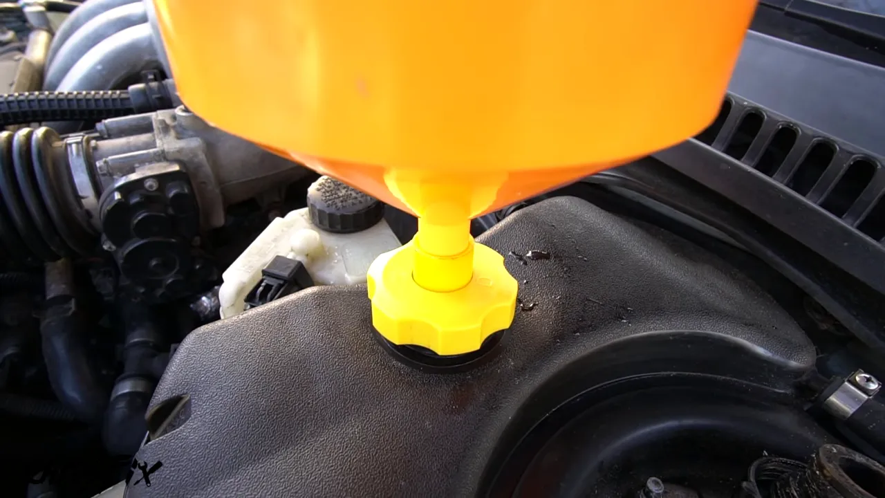 Orange spill-proof funnel attached to the Jaguar coolant reservoir with a yellow adapter