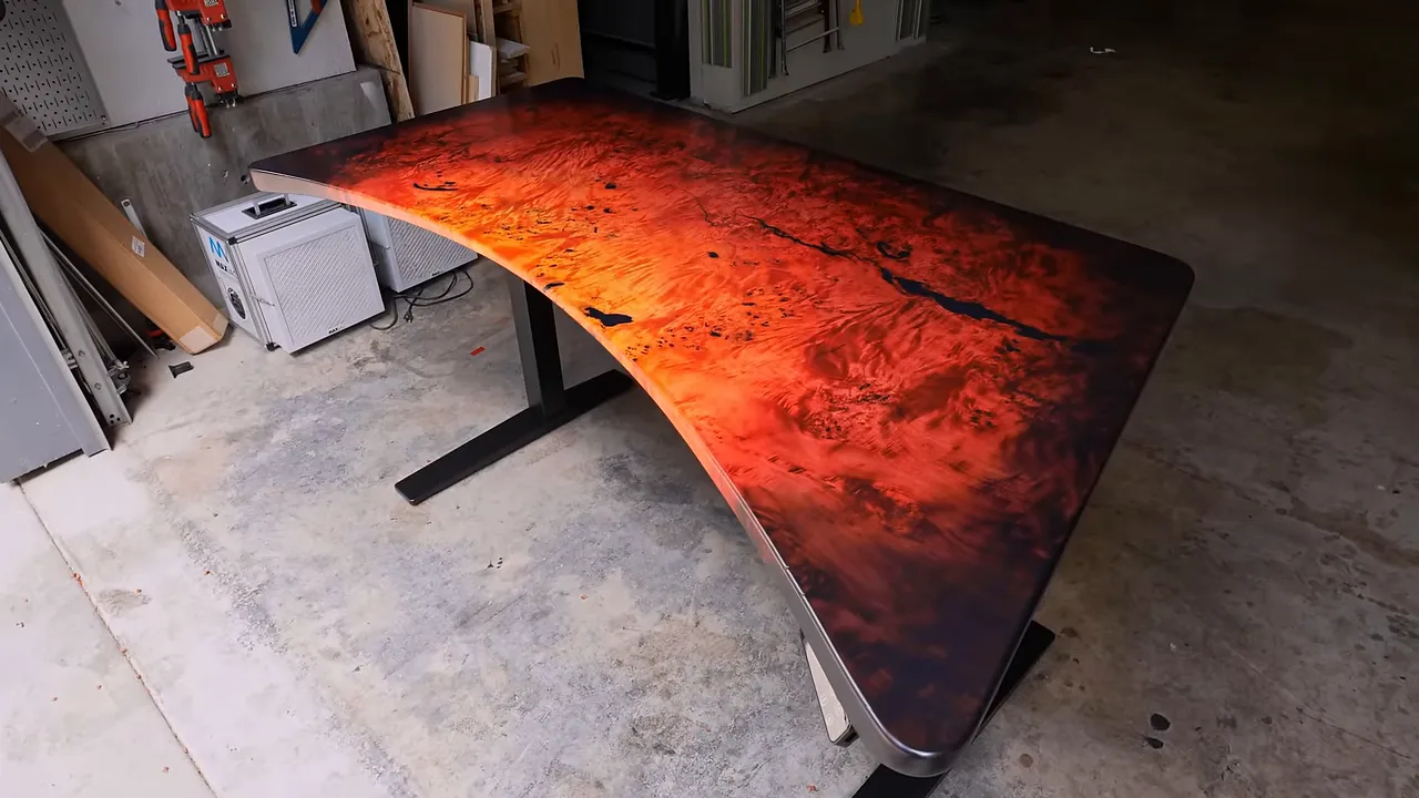 Finished red and orange curved burl desk mounted on a black standing desk base