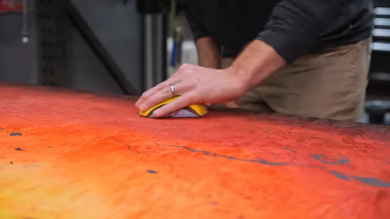 Hand sanding a red and orange dyed burl surface with a small yellow sanding block