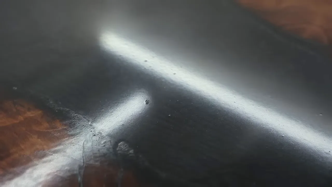 Close-up of a glossy dark finish with small raised specks beneath reflected shop lights