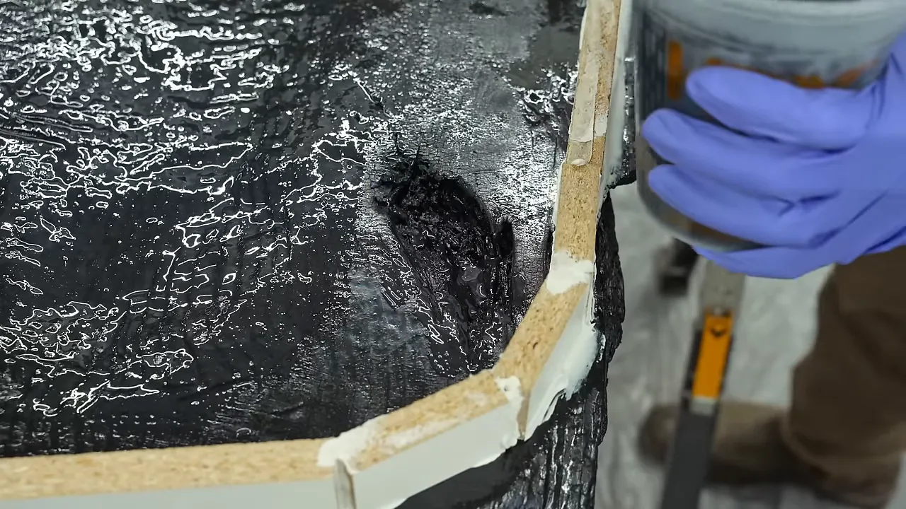 Brush applying dark metallic epoxy over textured char inside a narrow white form