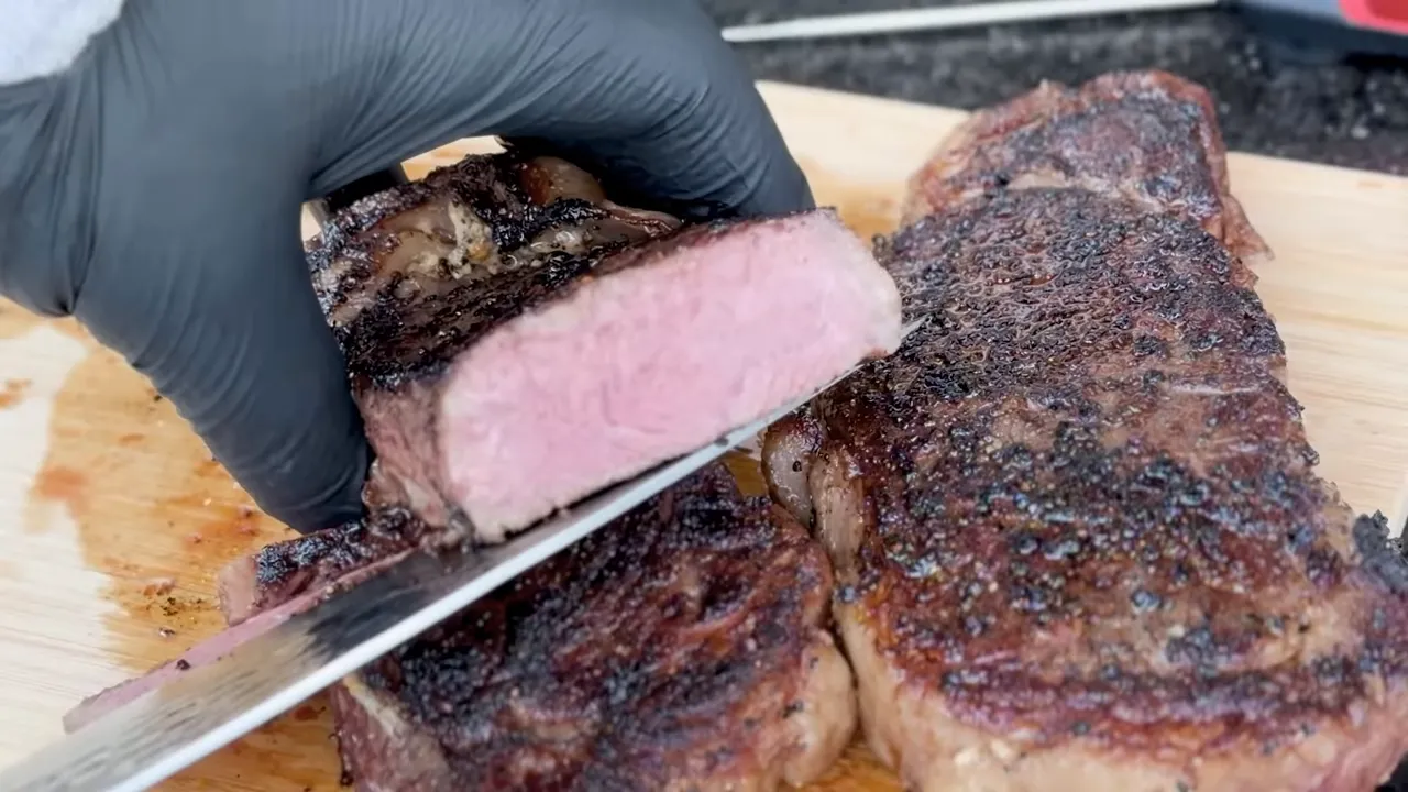 A sliced New York strip steak showing a pink interior beside another steak with a dark seared crust