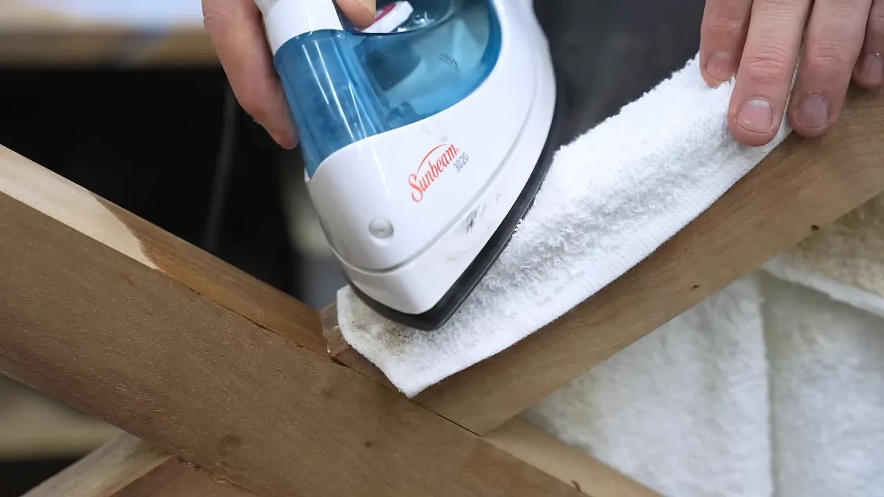 An iron pressing a wet white cloth against a walnut table leg