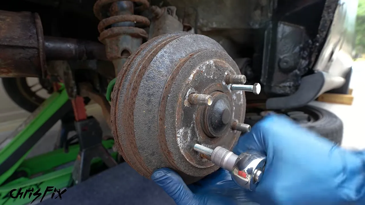 Two bolts threaded into removal holes in a rusty brake drum