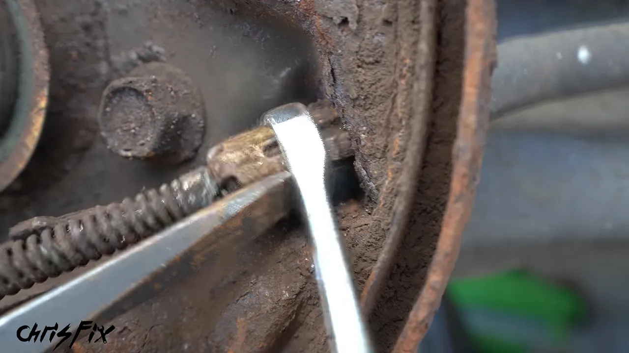 Box-end wrench fitted over the parking brake cable retaining fingers behind the backing plate