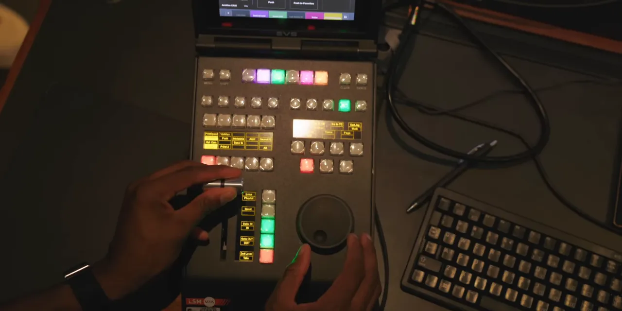 Overhead view of an EVS replay controller with a jog wheel, lever, illuminated buttons, and adjacent keyboard