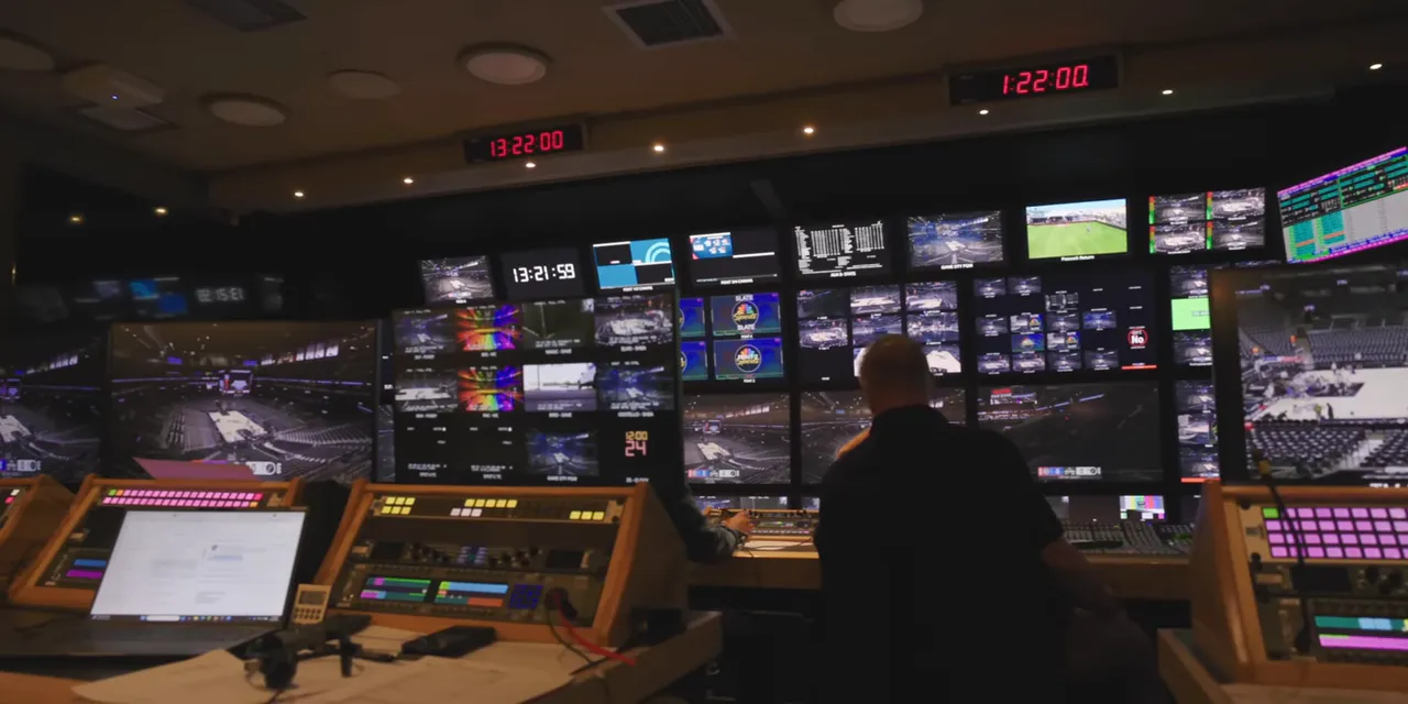 Interior of a broadcast production truck with operators, control consoles, and a wall of camera feeds