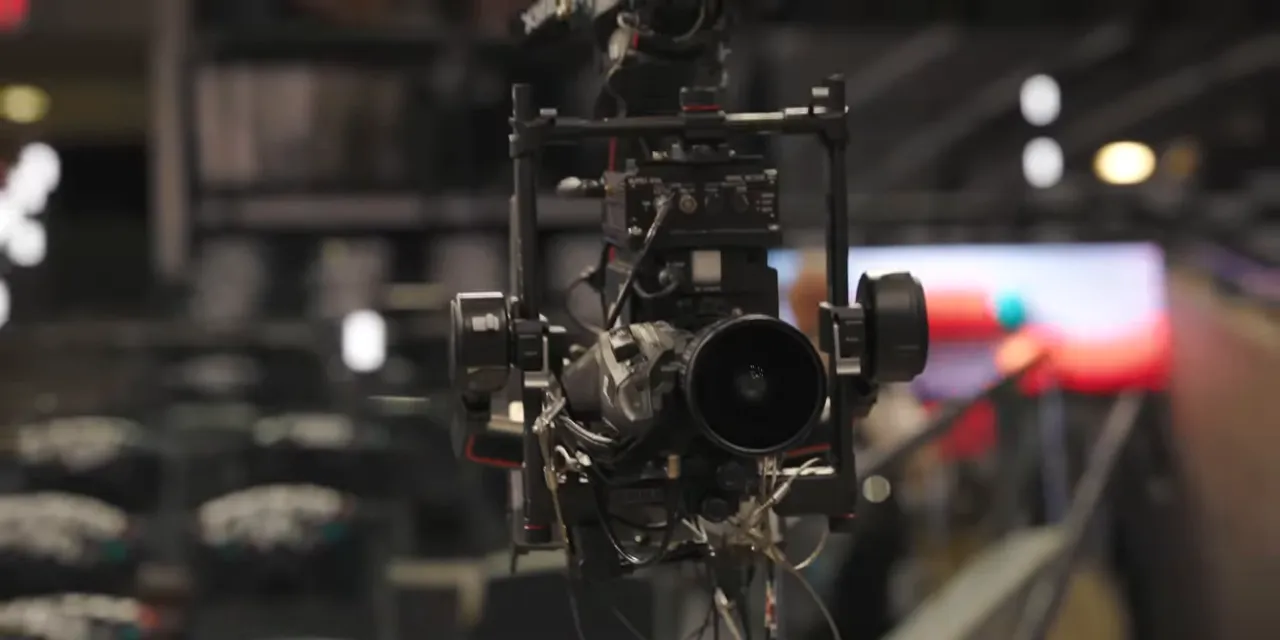 Camera and gimbal assembly suspended from cables inside the arena