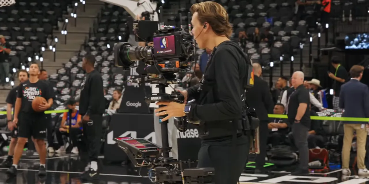 Camera operator wearing a waist-mounted support rig while holding a stabilized broadcast camera
