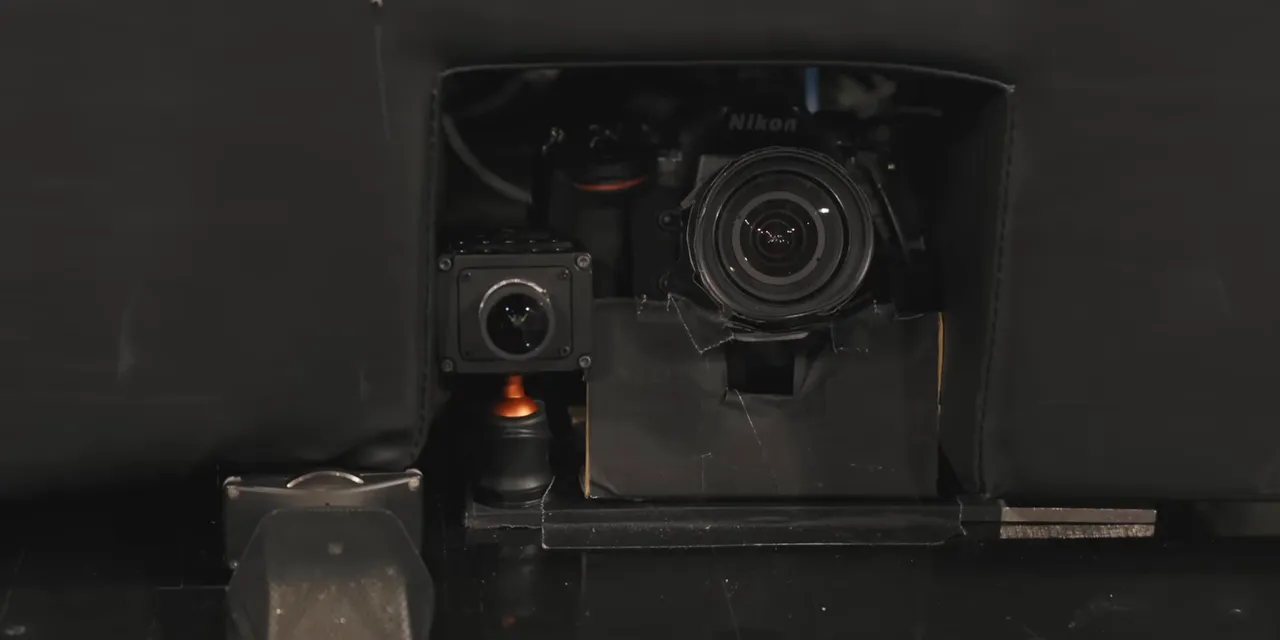 Camera lens and smaller device visible inside a cutout at the base of the basketball stanchion