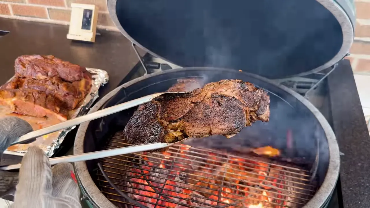 Tongs holding a browned steak over an open Big Green Egg