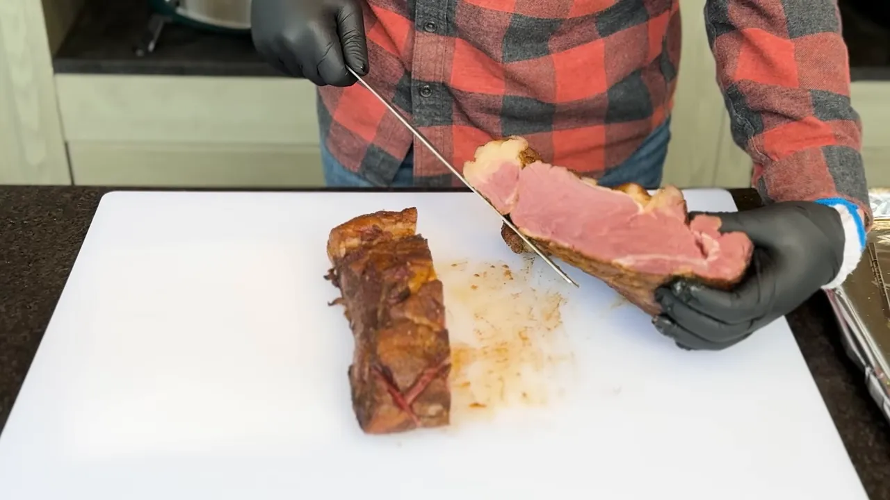 A thick slice of beef held above a cutting board showing a pink interior