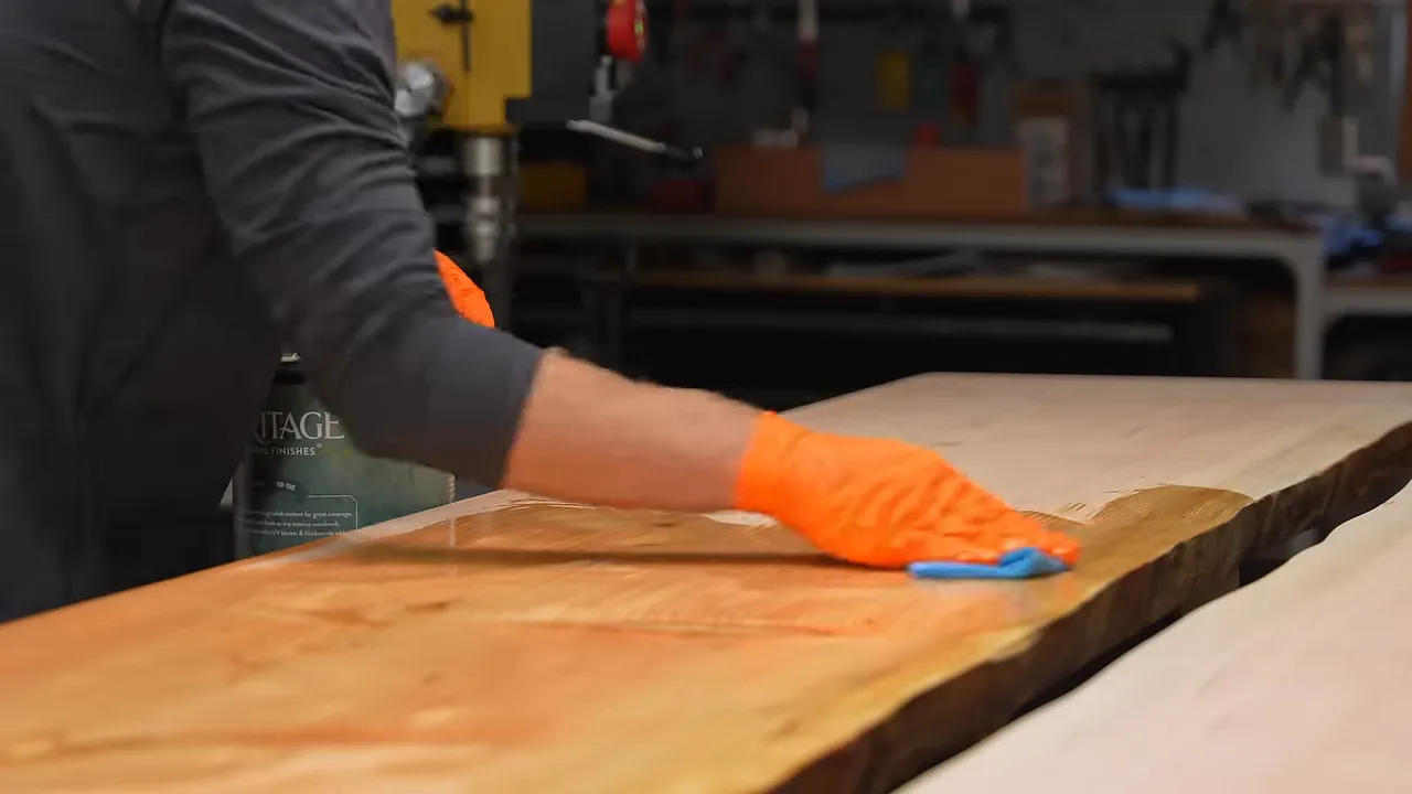 Orange-gloved hands wiping finish onto one of two long tabletop slabs